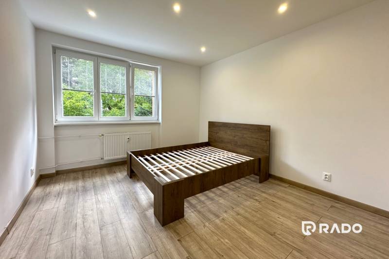 Bright bedroom with a wooden bed in a 2-room apartment with large windows.