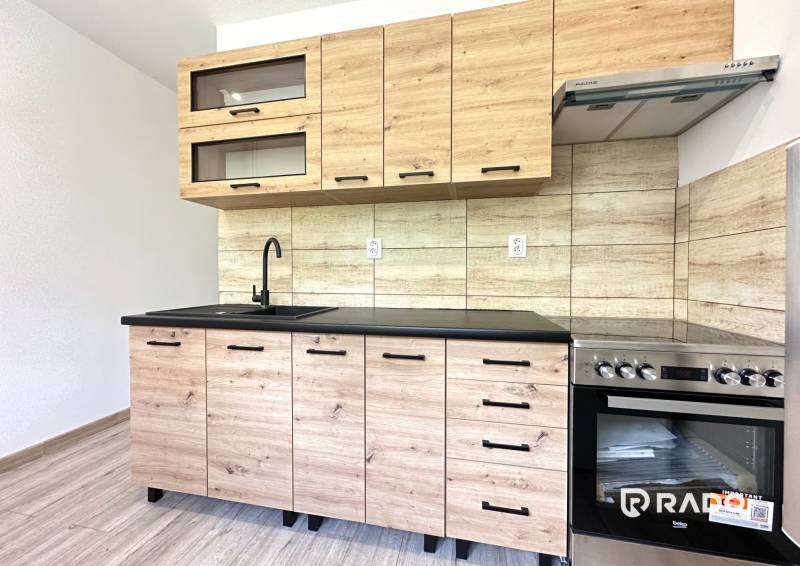 A kitchen with wooden paneling in a 2-room apartment, equipped with glass cabinets and a stove.