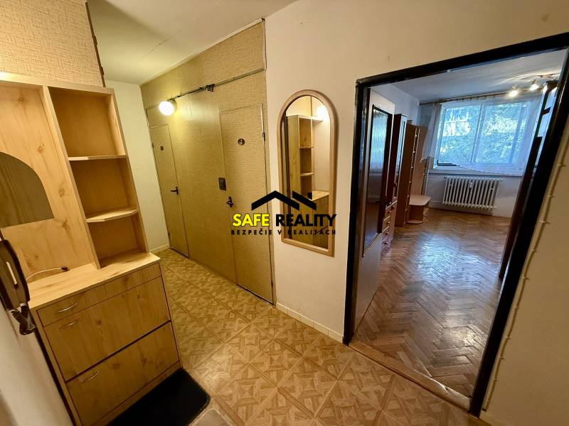A hallway with wooden furniture and a view into a room in a one-room apartment.