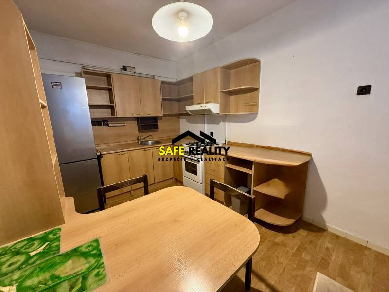 A kitchen in a one-room apartment equipped with wooden furniture and a refrigerator.