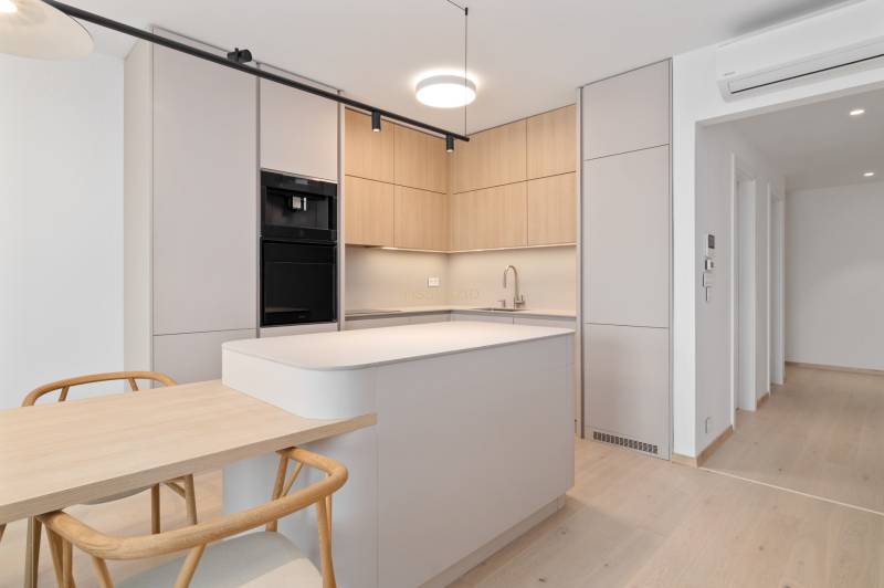 A kitchen in a 2-room apartment with wooden cabinets, a kitchen island, and a dining table.