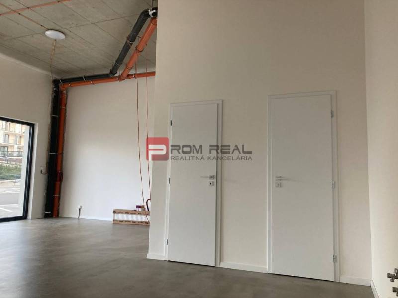 Empty commercial spaces with white doors and exposed pipes on the wall.