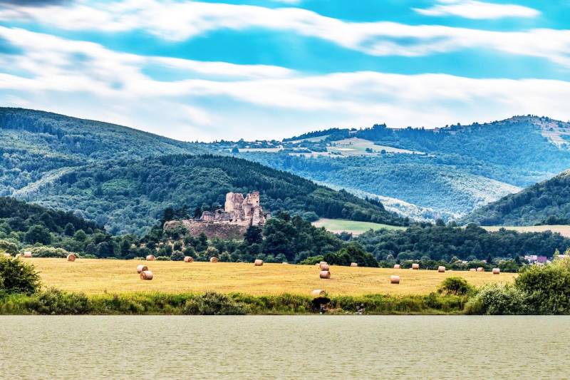 Picturesque scenery of agricultural and forest lands near Lučenec with castle ruins in the middle.