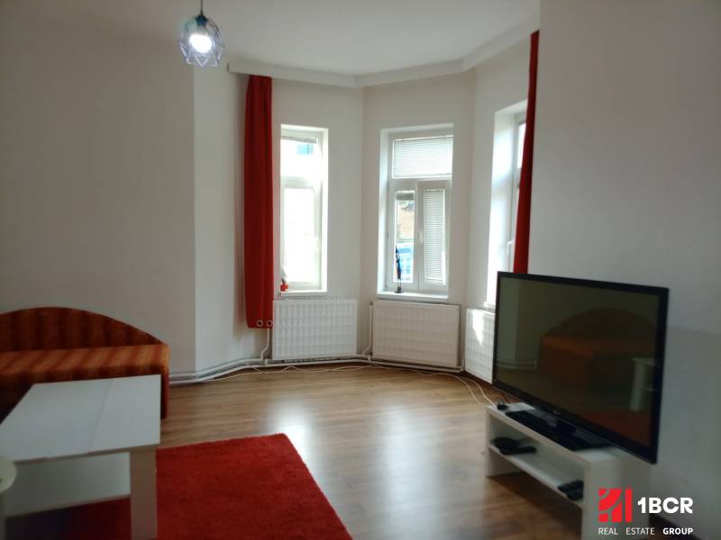 Living room with a sofa, television, table, and wooden decor flooring in a family house.