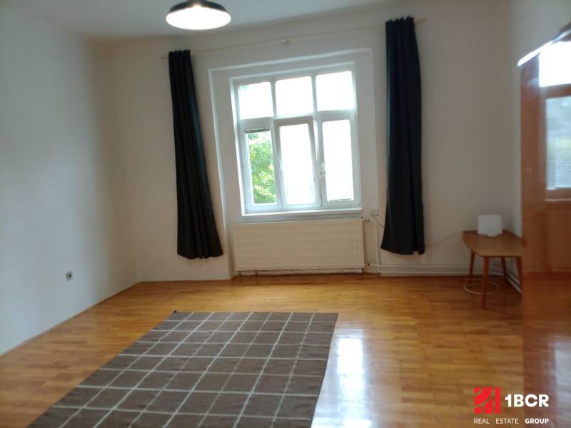 A room in a family house with a wooden decor floor, curtains, and a carpet.