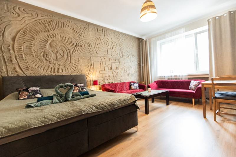 A room in a 2-room apartment with a bed, red sofas, and a decorative relief on the wall.