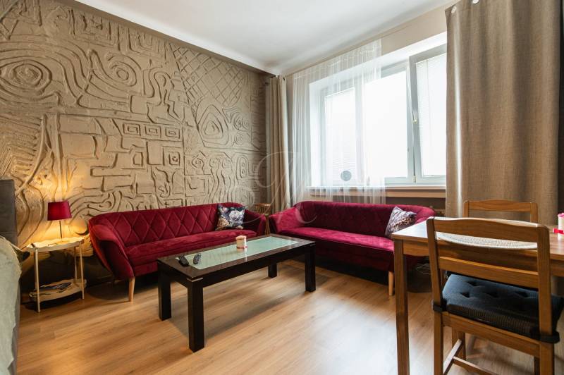 Living room in a two-room apartment with a patterned wall and red sofas.