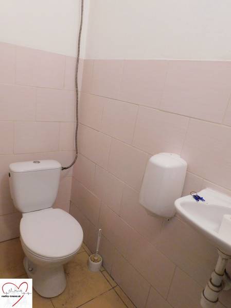 A restroom with a toilet, sink, and soap dispenser in an industrial building.