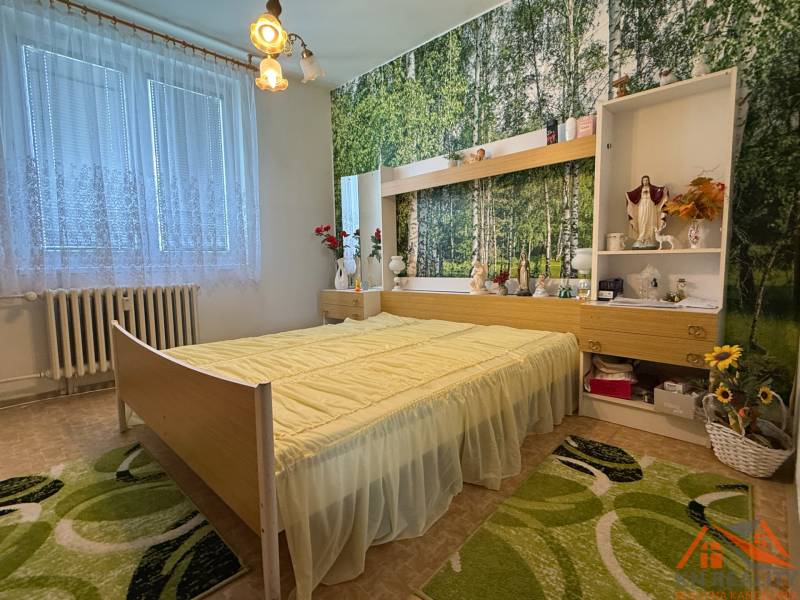 A bedroom in a three-room apartment with floral decorations and a forest wallpaper on the wall.