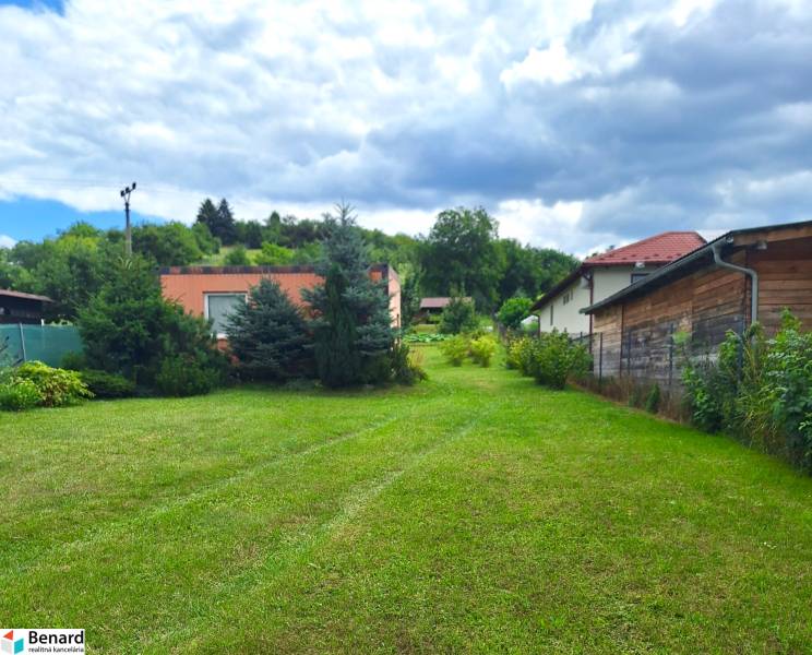 A grassy plot for living in the village of Bodovce surrounded by houses and trees.
