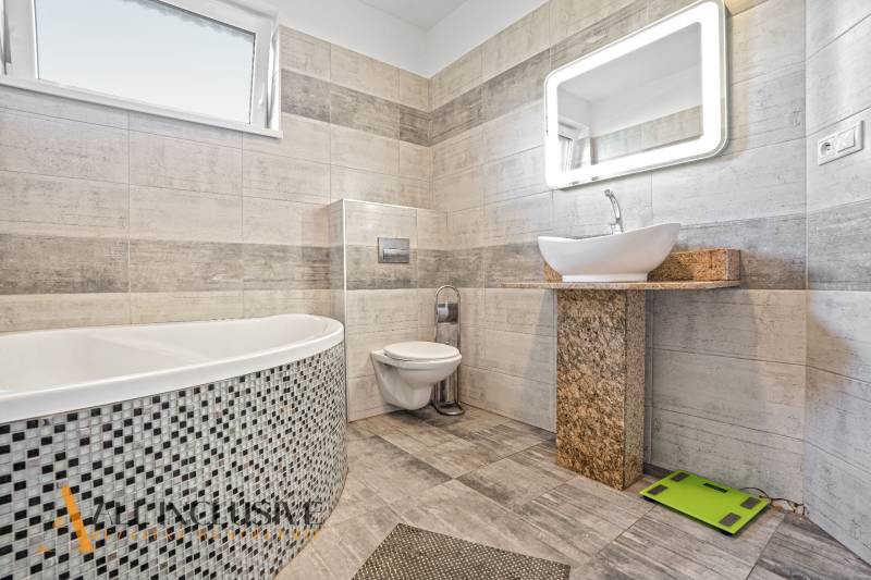 A bathroom in a family house with stylish ceramic tiles, a bathtub, and a designer sink.
