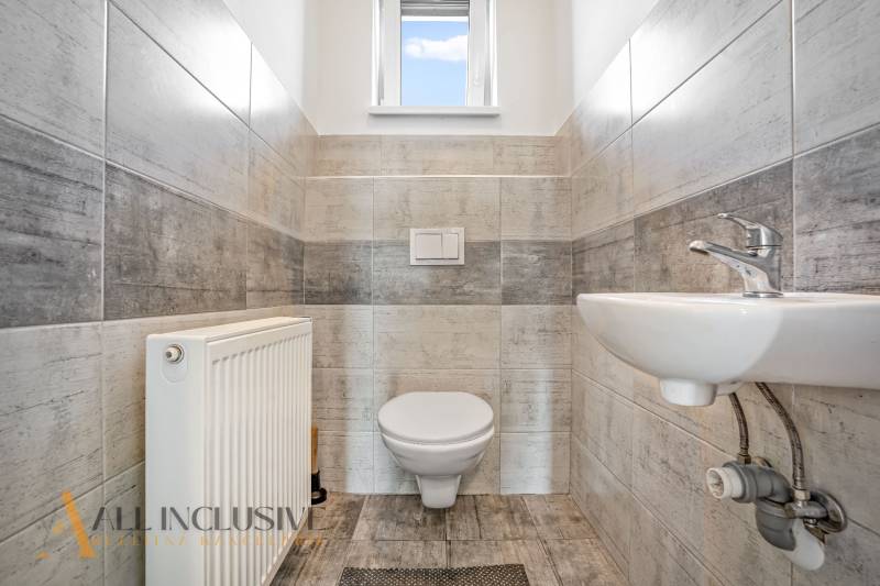 Bathroom in a family house with a toilet, sink, and radiator; light tiles.