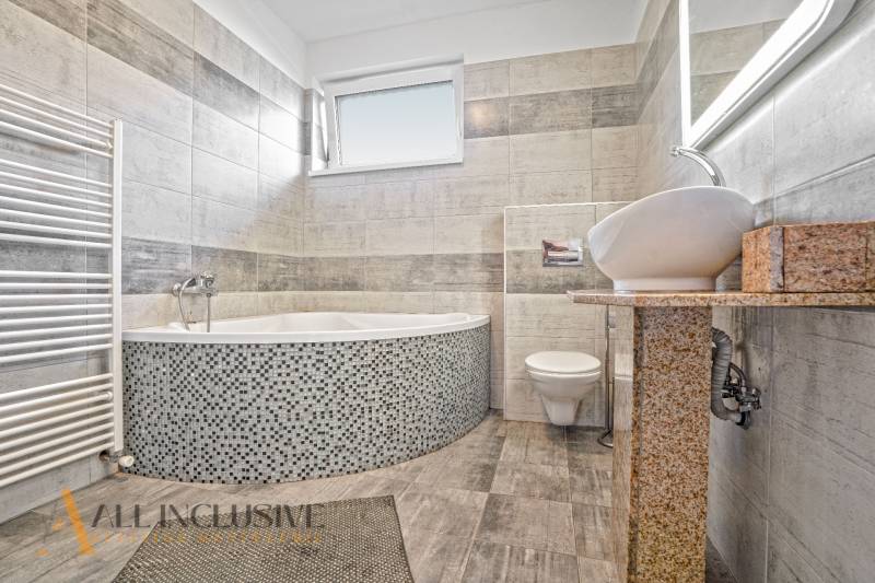 A bathroom in a family house with a bathtub, sink, and toilet, tiled with light tiles.