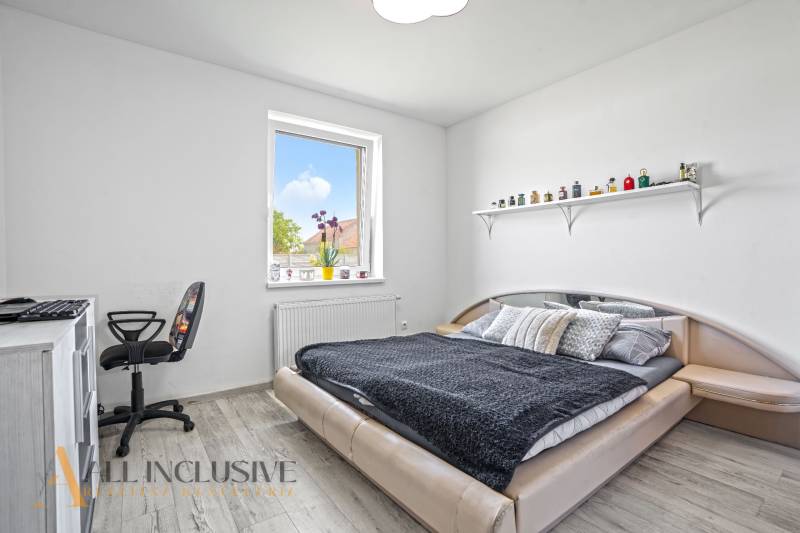 A bedroom in a family house with a bed, a chair, a table, and a shelf on the wall.