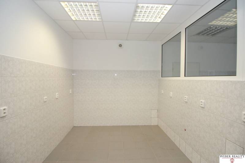 Commercial spaces with white tiles, a suspended ceiling, and windows.