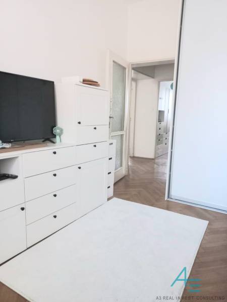 White living room in a 4-room apartment with a TV, cabinets, and wooden flooring.