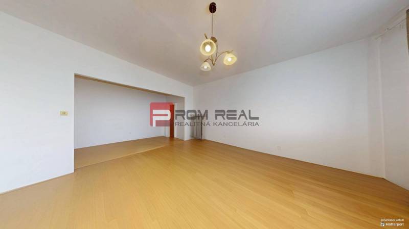 A spacious room with wooden flooring and a light fixture in a 3-room apartment.