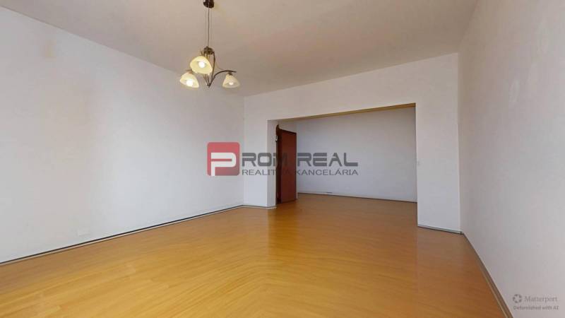 A spacious living room with wooden flooring and a chandelier in a 3-room apartment.