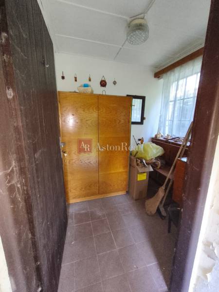 The interior of a cabin with a wooden wardrobe and a window, next to cardboard boxes and a broom.