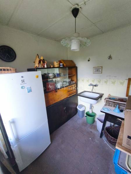 A kitchenette in a cottage with a sink, refrigerator, display cabinet, and a clock on the wall.