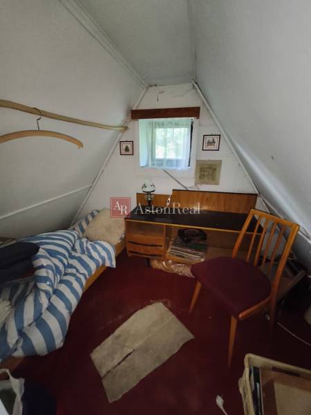 Attic room in a cottage with a bed, table, and chair, white wall.
