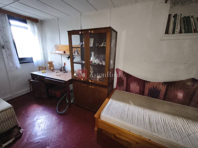 A room with a wooden floor, a wardrobe, a table, and a bed in a cabin.