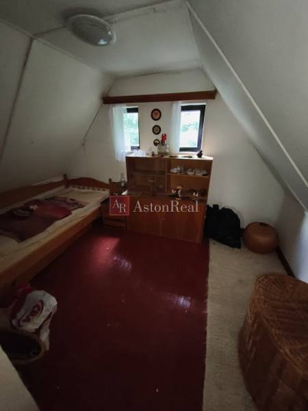 Attic room in a cottage with a bed, cabinet, and floor with wooden decor.