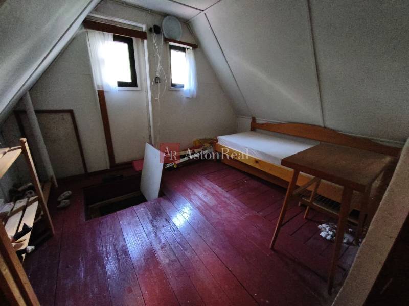 A room on the upper floor in a cottage with a wooden decor floor, simple furniture, and windows.