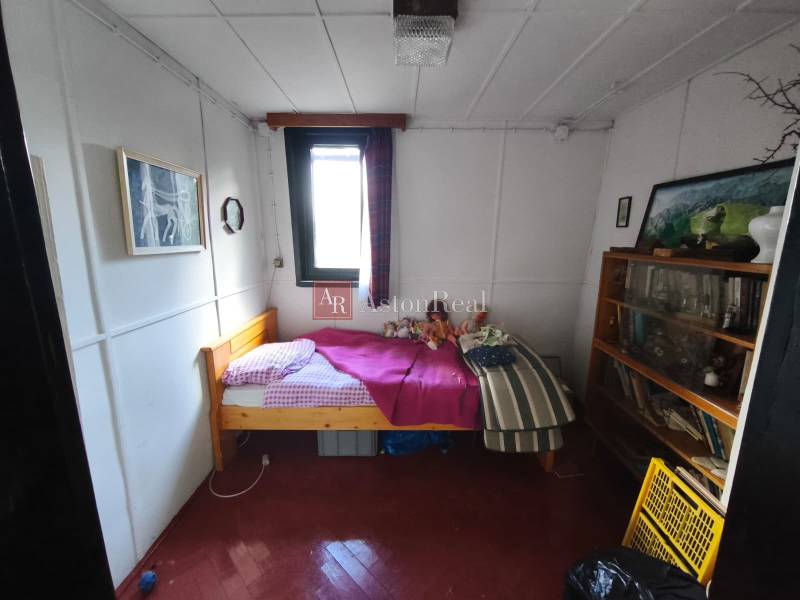 A room in a cottage with a bed, a bookshelf, and art pictures on the walls.
