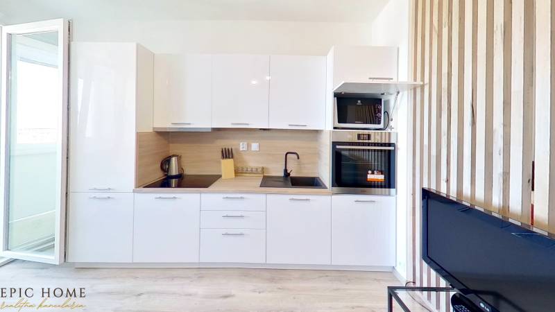 Kitchen in a studio apartment with a white kitchen unit, stove, oven, and open balcony doors.
