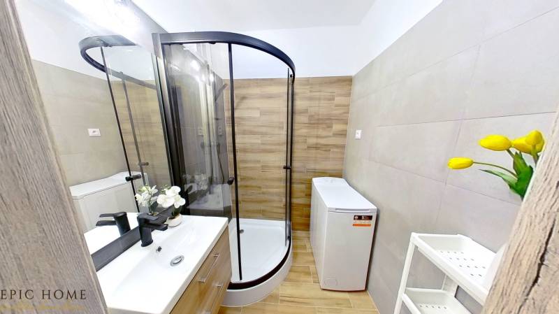 Bathroom with a corner shower, washing machine, and sink in a studio apartment.