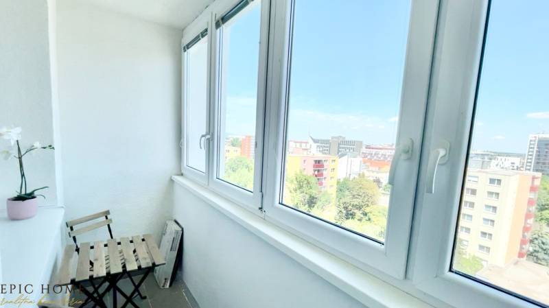 A glazed balcony with a view of Bratislava, a potted plant, a chair, and a table.