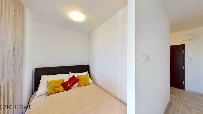 A bedroom with a double bed, white walls, and colorful pillows in a studio apartment.