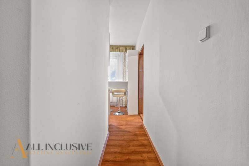 A narrow hallway in a 2-room apartment with wooden flooring and light-colored furniture.