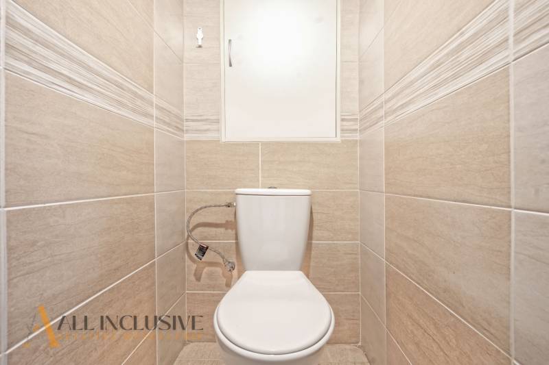 A toilet with beige tiles in a 2-room apartment.