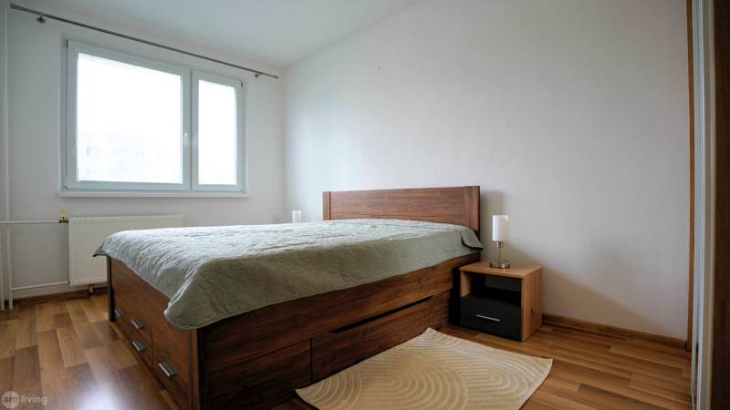 Bedroom in a two-room apartment with wooden flooring and a bed with storage space.