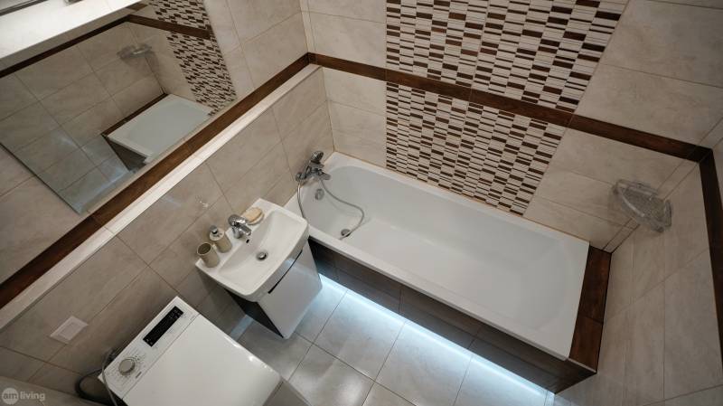 Bathroom in a 2-room apartment with a bathtub, mirror, sink, and washing machine.