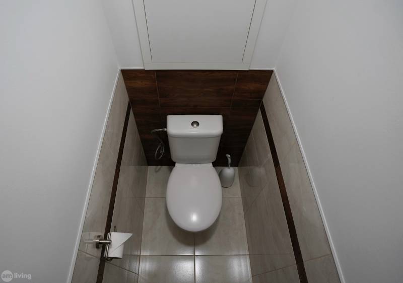 A bathroom with white sanitary ware in a 2-room apartment, clad in dark wood and tiles.