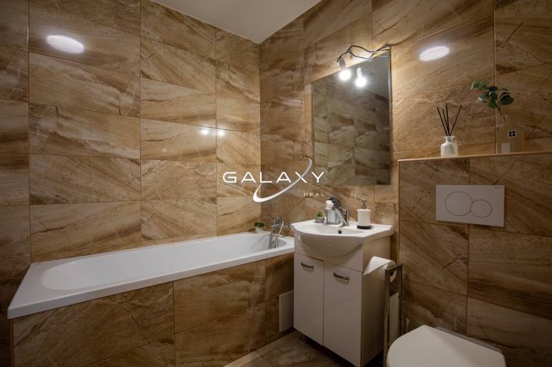 Bathroom in a family house with a bathtub, sink, and beige tiles in warm tones.