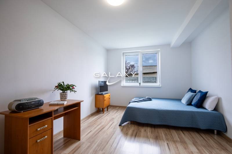 A room in a family house with a bed, a desk, and a television on a light floor.