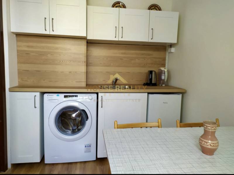 A kitchen in a studio apartment with white cabinets, a washing machine, a sink, and a dining table.