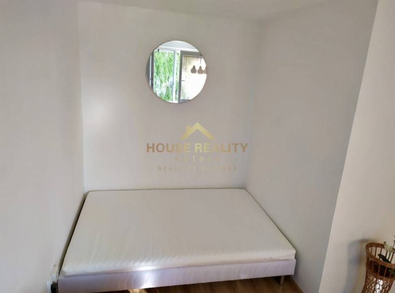 One bed, round mirror, and wooden floor in a studio apartment.
