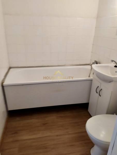 Bathroom in a studio apartment with a bathtub, sink, and toilet, wood-look tiles.