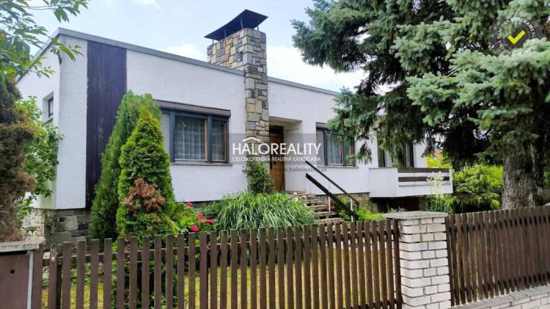 A family house in Plavecký Mikuláš, surrounded by trees and a front garden, with a stone chimney.