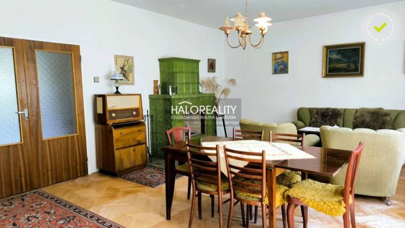 Living room in a family house with wooden furniture, a green tiled stove, and paintings on the walls.