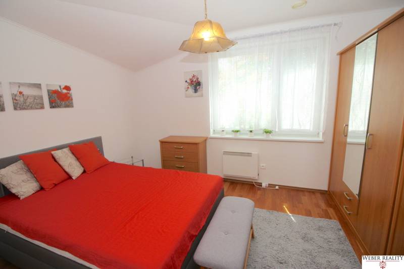 A bedroom in a family house with red bedding, a dresser, and a large window.