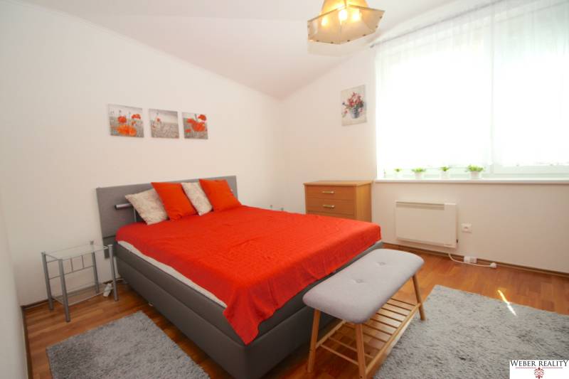 A bedroom in a family house with a gray bed, red blankets, and wooden furniture.