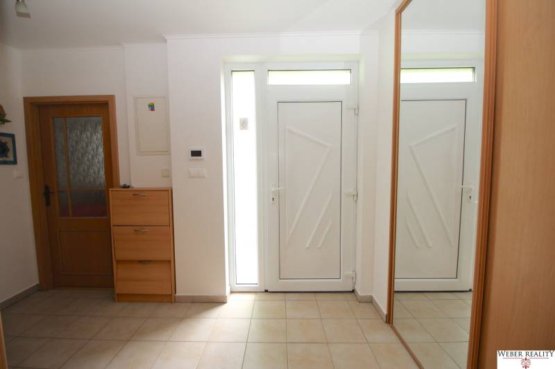 The entrance hall of a family house with white doors, a mirror, and a wooden shoe cabinet.