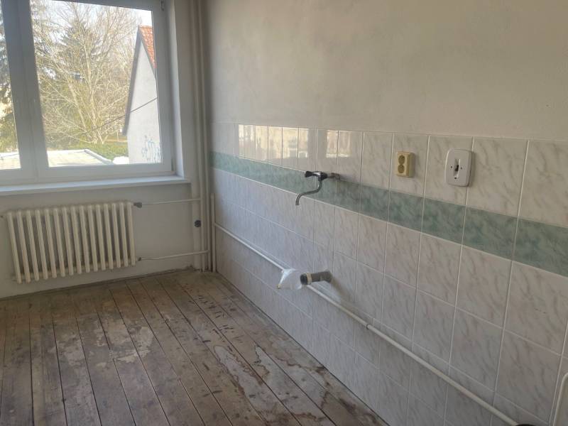 An empty kitchen in a family house with tiles and wooden flooring.