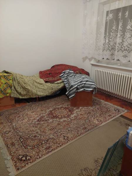 A room in a family house with a bed, carpet, and lace curtains.
